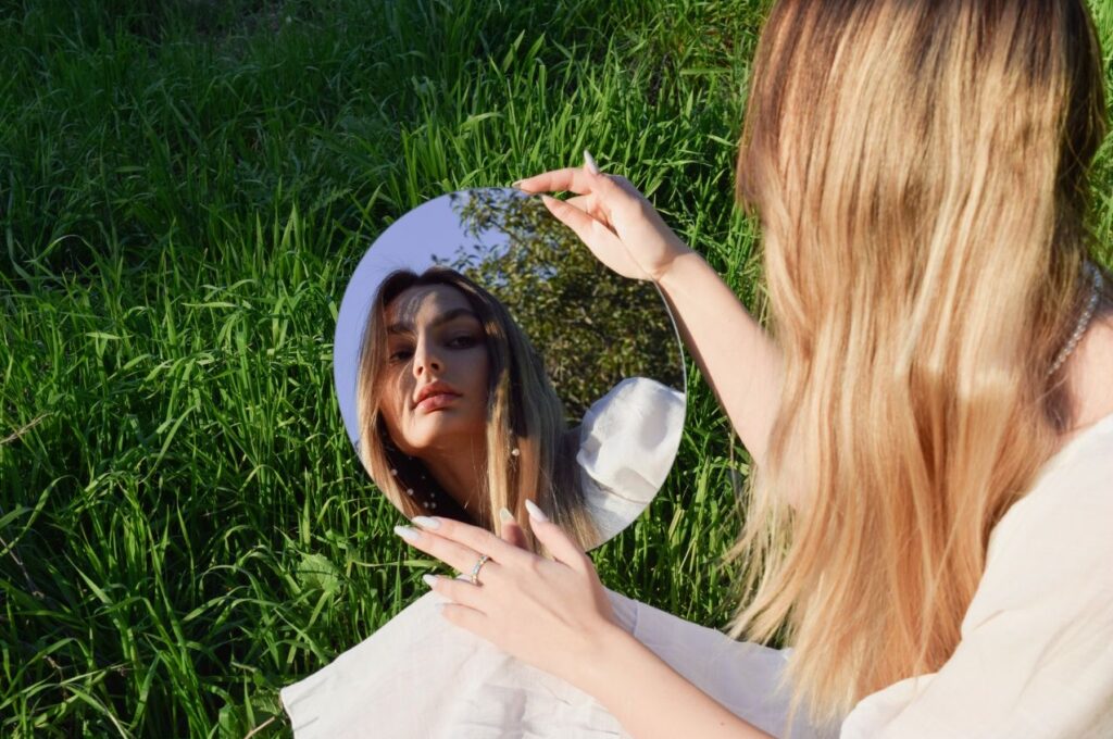 A woman gazing at herself through a mirror in a field of grass. Sustainability